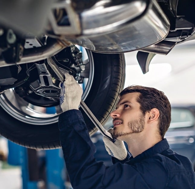 A man is working underneath a car, focused on repairs near the wheel